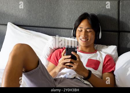 Listening to music with headphones, smiling teenager using smartphone on bed Stock Photo