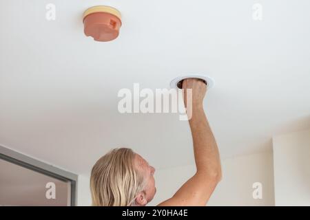 A man replaces an LED light bulb in a ceiling light. Stock Photo