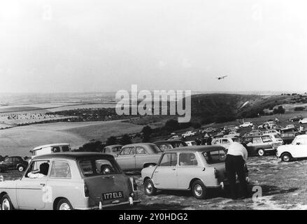 1966 archive. People in cars of the period on Dunstable Downs, Chiltern Hills looking down onto an air event taking place at the London Gliding Club airfield below. Glider on approach to land over hills Stock Photo