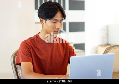 Working on laptop, young asian man concentrating on task in modern office setting Stock Photo