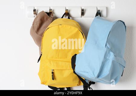 Bright backpacks and cap hanging on white wall Stock Photo