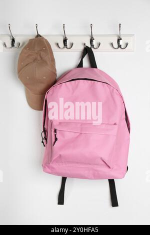Pink backpack and cap hanging on white wall Stock Photo