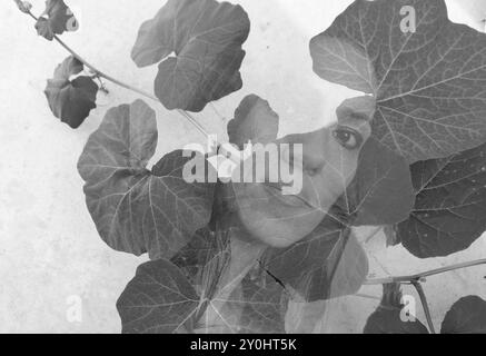 Abstract monochrome double exposure image of a young woman's face obscured by leaves of a plant - headshot with plant overlay Stock Photo