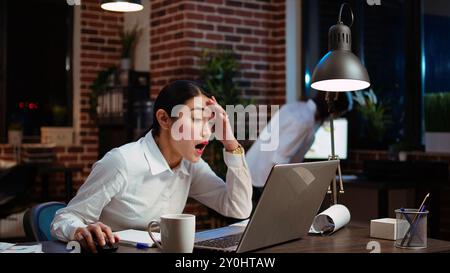 Company accountant stressed by complicated sales report needed to plan business development. Office employee sighing in frustration, feeling overworked while using laptop to do project research Stock Photo
