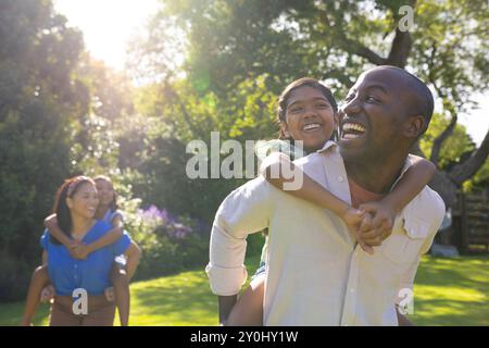 Playing piggyback, happy family enjoying outdoor time together in backyard Stock Photo