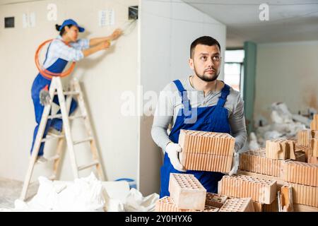 Man builder carrying bricks in construction site in apartment Stock Photo