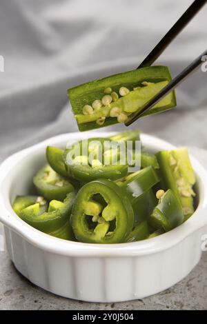 A food photograph of a bowl of sliced peppers and a pair of chopsticks holing a slice Stock Photo