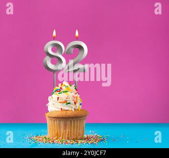 Lit birthday candle with the number 82 - Celebration card on violet and blue background Stock Photo