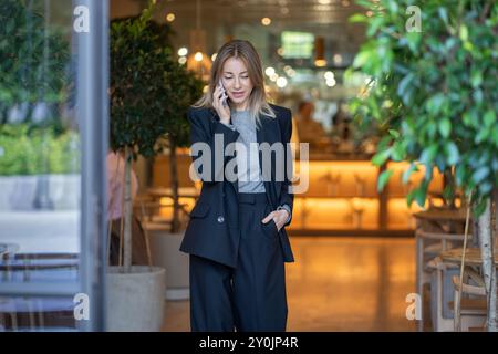 Focused on phone call confident pleased woman cafe owner remotely resolves small business issues. Stock Photo