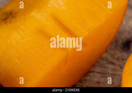 Half-ripe orange persimmon, fresh ripe persimmon cut into pieces on a cutting board with a sharp knife Stock Photo