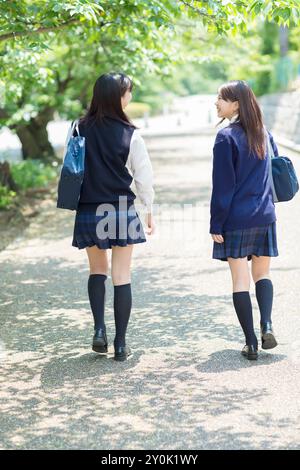 Two Japanese high school girls walking down a tree lined road Stock Photo