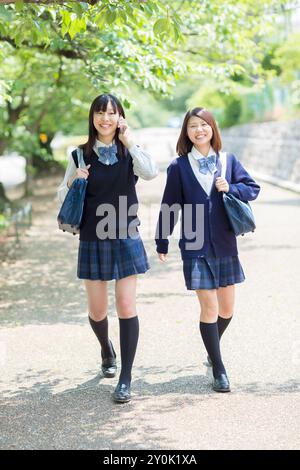 Two Japanese high school girls walking down a tree lined road Stock Photo