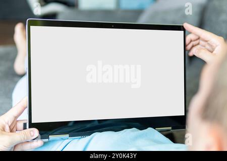 man lies on a sofa at home and looks at the screen of a modern ultrabook transformer. blank screen for design. empty black monitor for text Stock Photo