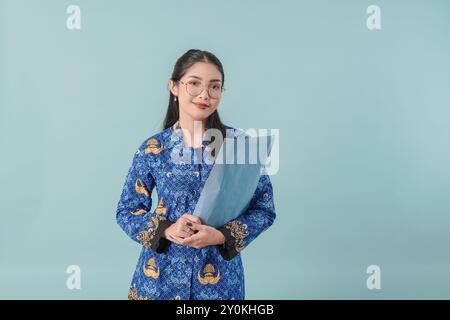 Beautiful government worker woman in blue batik uniform and glasses holding a document and looking at camera. PNS civil servant concept. Stock Photo