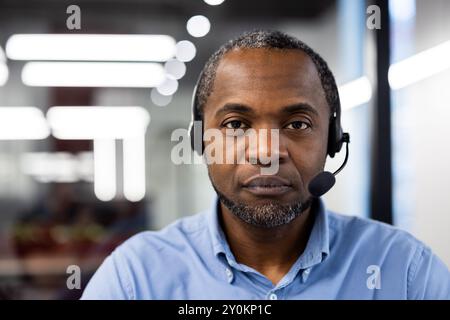 Serious businessman wearing headset in modern office setting. Focused on communication and technology, highlighting professional work environment. Stock Photo