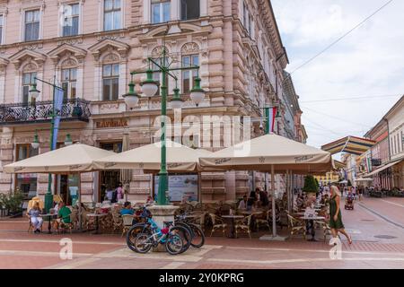 People sat outside a cafe - al fresco - in the centre of the Hungarian city of Szeged on a cloudy summer day, with bikes parked against a street lamp. Stock Photo