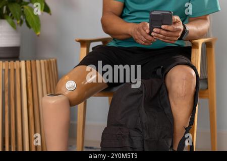 Man with prosthetic leg sitting and using smartphone, backpack on lap Stock Photo