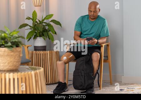 Man with prosthetic leg sitting and using smartphone, sitting in waiting room Stock Photo