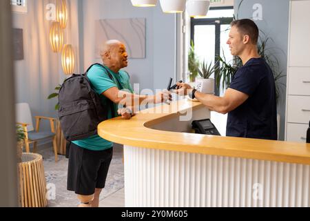 Man with prosthetic leg checking in at reception desk, handing ID to receptionist Stock Photo
