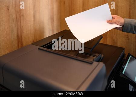 Cropped hand of young businessman holding blank white paper and using photocopier machine in office Stock Photo