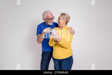 Cheerful senior couple looking at each other and reading good news over phone on white background Stock Photo