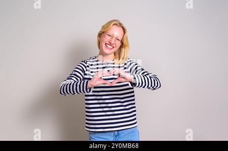 Portrait of ecstatic young woman gesturing heart shape and smiling at camera on white background Stock Photo