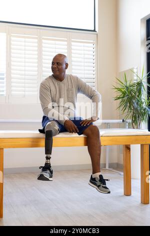 Man with prosthetic leg sitting on table, smiling and looking away Stock Photo