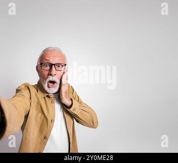 Worried senior businessman touching face and looking at camera in shock against white background Stock Photo