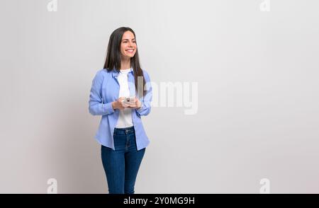 Confident young female entrepreneur messaging over cellphone and looking away on white background Stock Photo