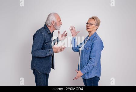 Frustrated senior wife looking away and ignoring angry husband arguing with her on white background Stock Photo