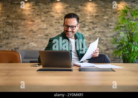 Positive male professional smiling and analyzing report over computer while working at desk in office Stock Photo
