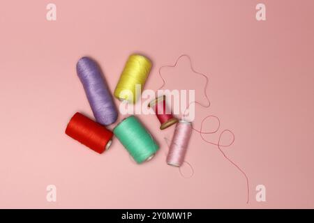 Spools of thread and needles on a pink background with space for text, top view photo of sewing supplies. Stock Photo