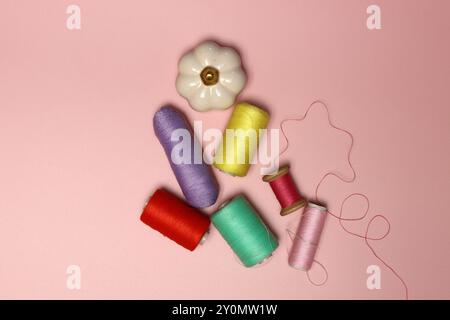 Spools of thread and needles on a pink background with space for text, top view photo of sewing supplies. Stock Photo