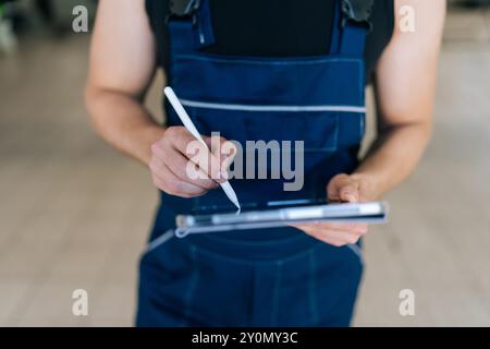 Closeup cropped shot of unrecognizable mechanic male holding digital tablet and using stylus. Close-up of auto mechanic man servicing car, checking Stock Photo