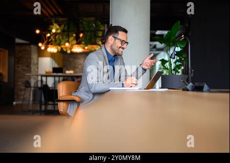 Male IT programmer smiling and discussing project online over video call on laptop at his workplace Stock Photo