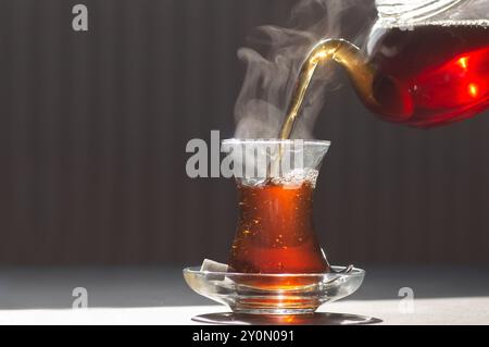 Glass cup of brewed black turkish tea pouring from teapot, traditional hot drink concept Stock Photo