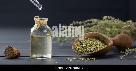 Glass bottle of thyme essential oil and bunch of dry thyme on black wooden rustic background, oil dripping Stock Photo