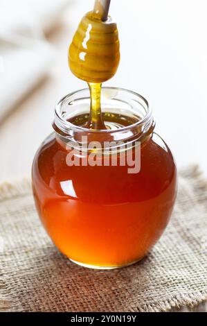 Organic fresh liquid honey in glass jar or bowl with dipper on rustic background, healthy food Stock Photo