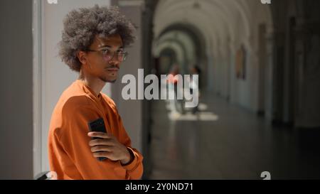 African American student guy using mobile phone in university hall corridor near window looking holding smartphone app chatting internet education Stock Photo