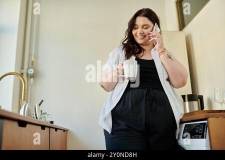 A plus size woman smiles while holding a mug and chatting on the phone. Stock Photo