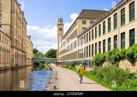 Woman walking along the canal at Salts Mill on the Leeds and Liverpool Canal Saltaire Village Bradford, West Yorkshire England UK GB Europe Stock Photo