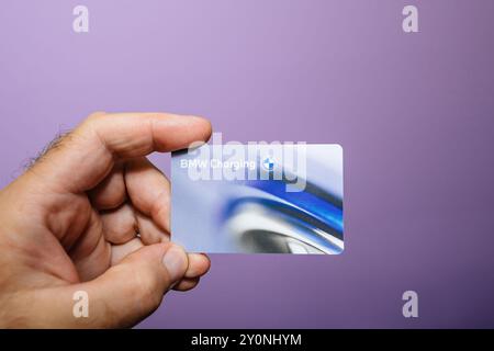 Munich, Germany - Sep 2, 2024: A male hand presents the BMW charging card for electric vehicles against a purple background, emphasizing advanced technology and modern automotive solutions Stock Photo