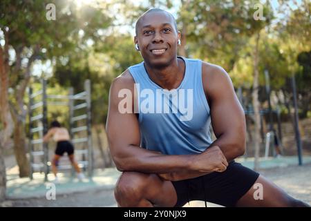 African athletic man dressed in sleeveless blue shirt, black shorts do leg stretch or warming up exercise in public park in sunny summer day. Sport Stock Photo