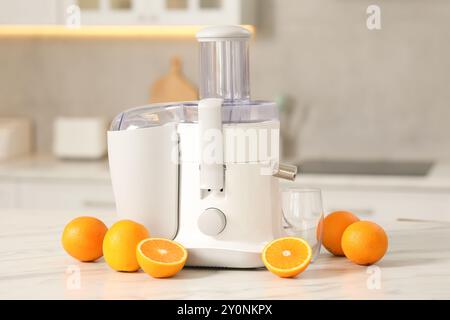 Modern juicer, oranges and glass on white marble table in kitchen Stock Photo