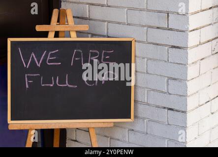 We Are Full Up sign on blackboard white brick background Stock Photo