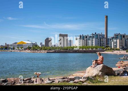 Woman sitting on a rock reading at Eiran ranta on sunny Midsummer's Eve in Eira district of Helsinki, Finland Stock Photo