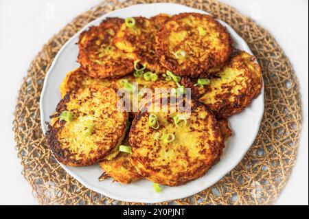 Fried salty pancake from potato, carrot and zucchini on white plate on bamboo pad, closeup. Stock Photo