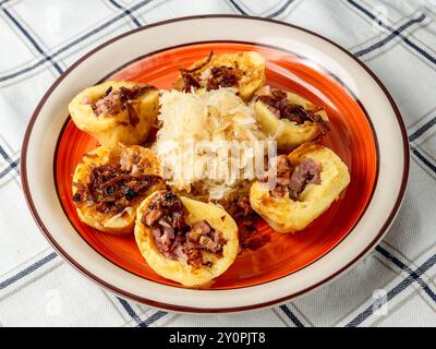 Boiled dumpling stuffed with smoked meat sprikled with sweet roasted onion, sauerkraut on red plate pn white checkered tablecloth, closeup. Czech repu Stock Photo