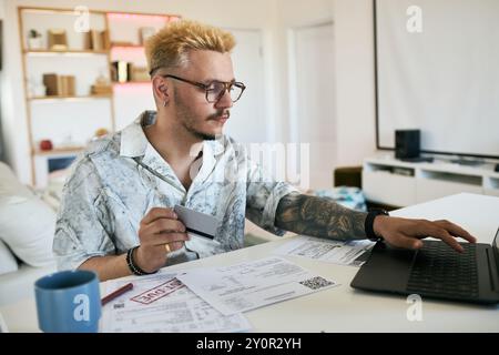 Focused young man analyzing documents and using laptop while working in modern home office setting Stock Photo