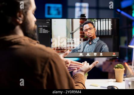 Cybersecurity professional helped by coworker during internet videocall to look for company security loopholes and injected viruses. Engineer and colleague in remote videoconference writing code on PC Stock Photo